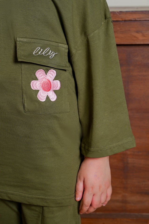 Green jacket with a pink flower patch and 'lily' embroidery on a wooden surface