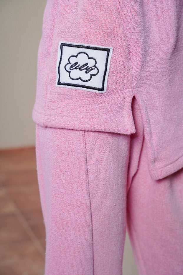 Pink fleece pants with a cloud logo on the pocket against a neutral background