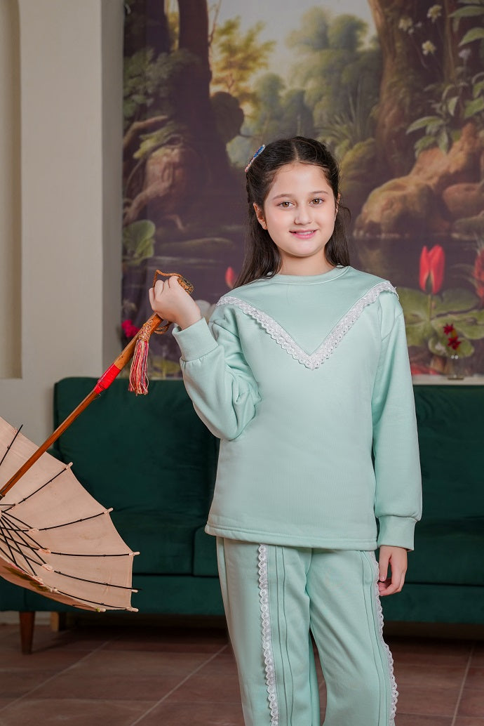 Young girl in a light green outfit holding a parasol in a room with a painting of a landscape.