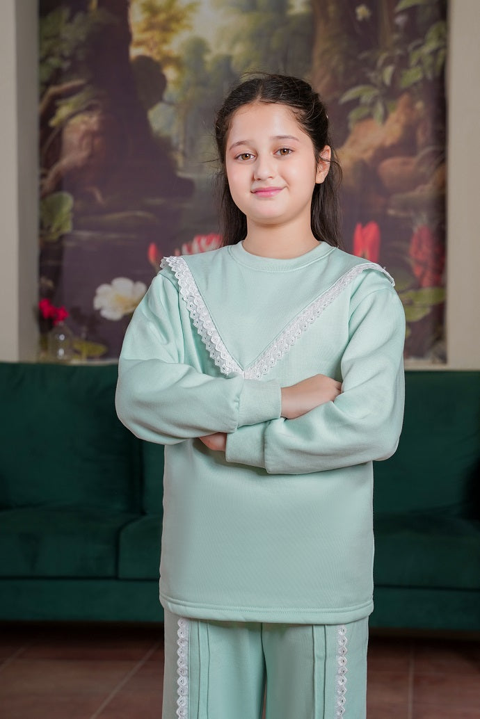 Person wearing a light green outfit with lace details in a room with a green couch and floral wall art.