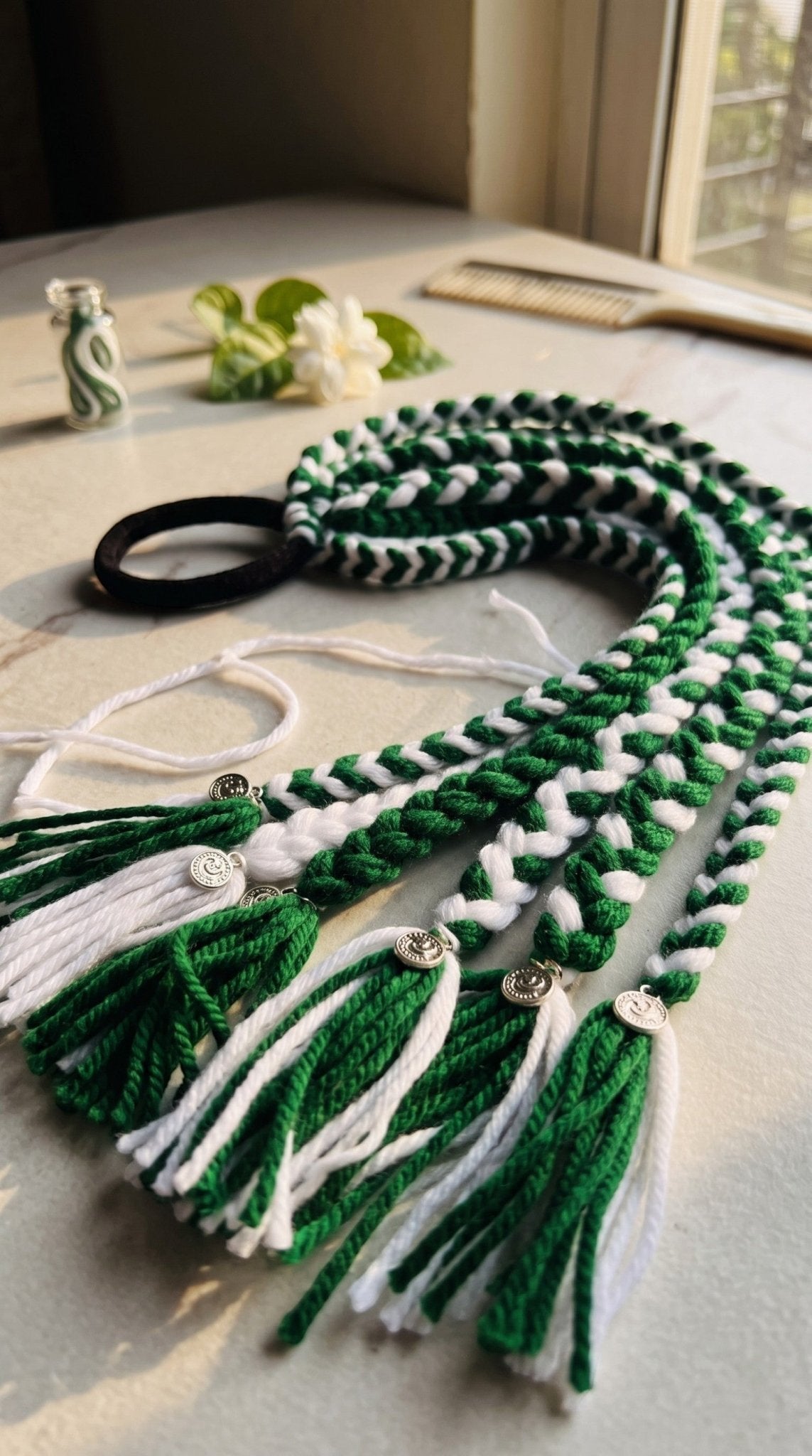 Lily green and white hand-braided yarn hair accessory with metallic charms on a black hair tie for a festive look.