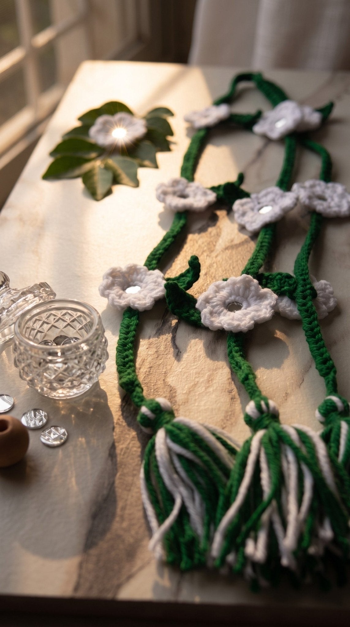 Lily green and white crocheted flower hair braids with mirror centers and multi-tonal tassels on a marble surface.
