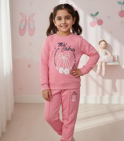 Young girl in a pink outfit standing in a room with a doll and ballet shoes on the wall.