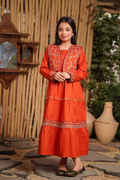 Girl in an orange traditional outfit standing in front of a rustic wooden wall.