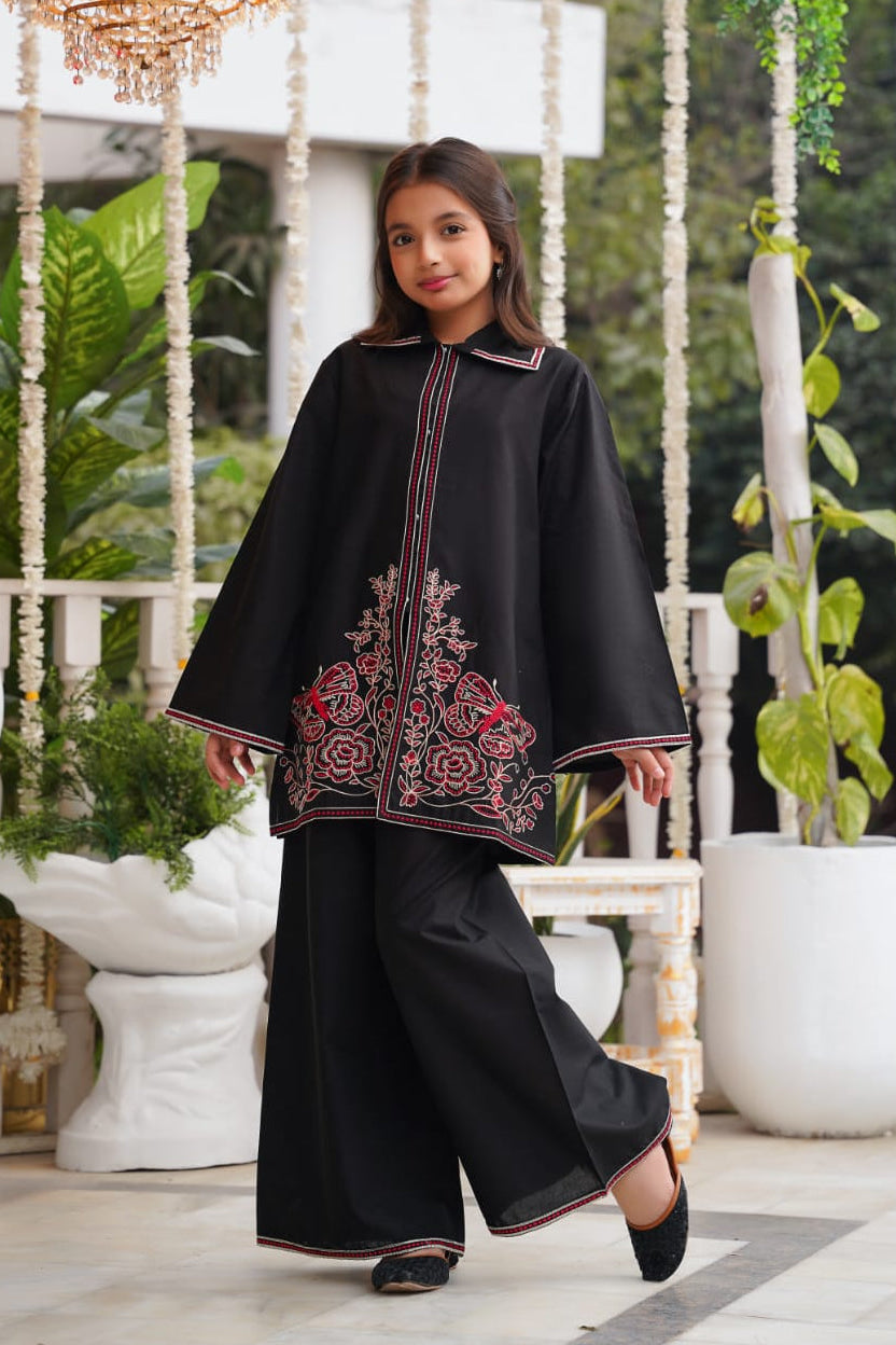 Girl wearing a black embroidered poncho in an indoor setting with plants and a chandelier.