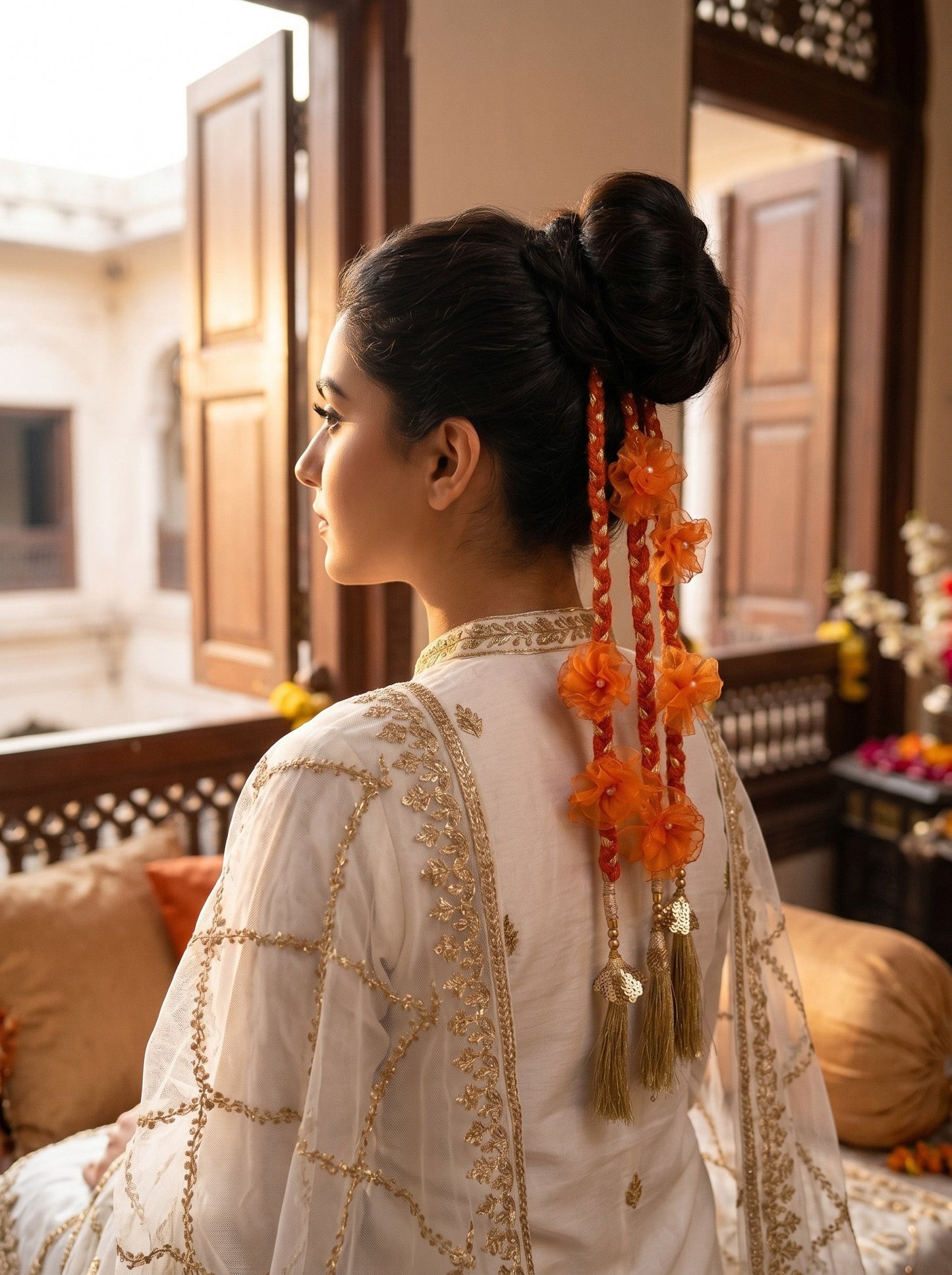 Lily Aamrass Blossom Paranda in orange with floral accents and gold tassels worn in a braided bun hairstyle.