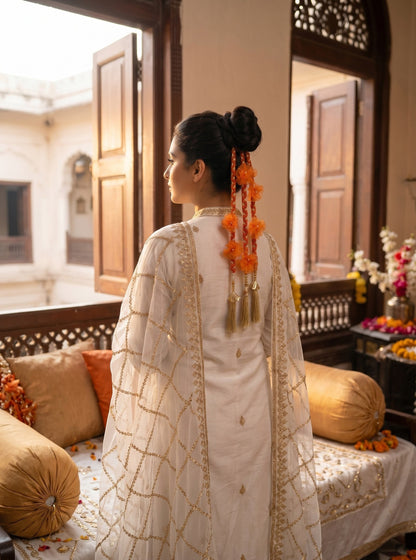 Lily Aamrass Blossom orange floral paranda with gold tassels worn in a bun by a woman in traditional white attire