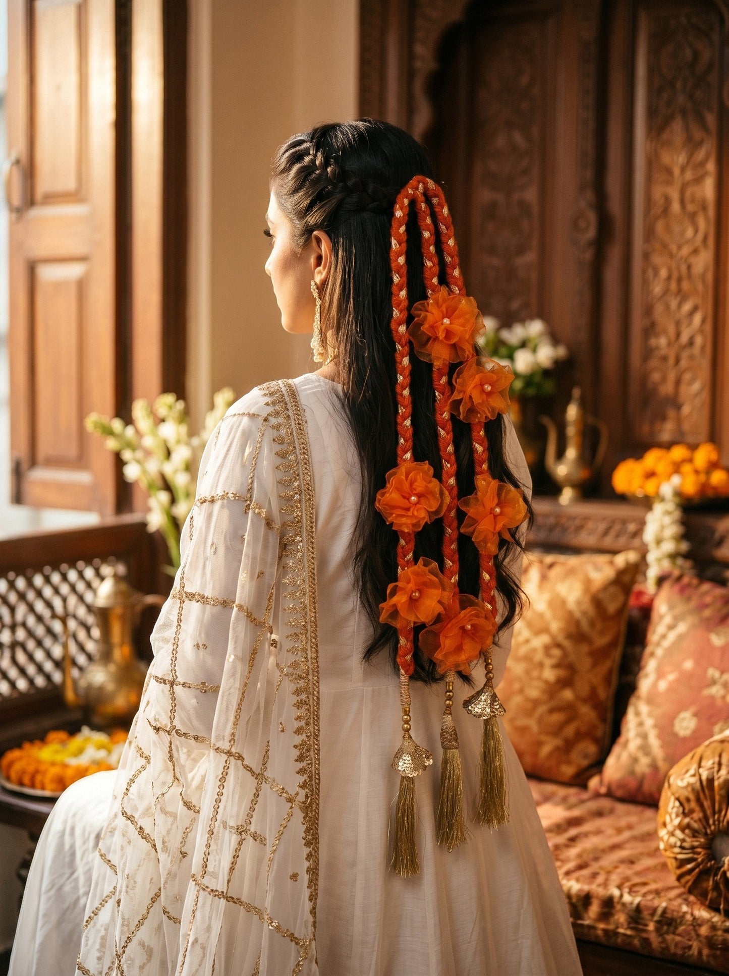 Lily Aamrass Blossom Paranda featuring vibrant orange floral embellishments and gold-toned tassels on a braided hairstyle
