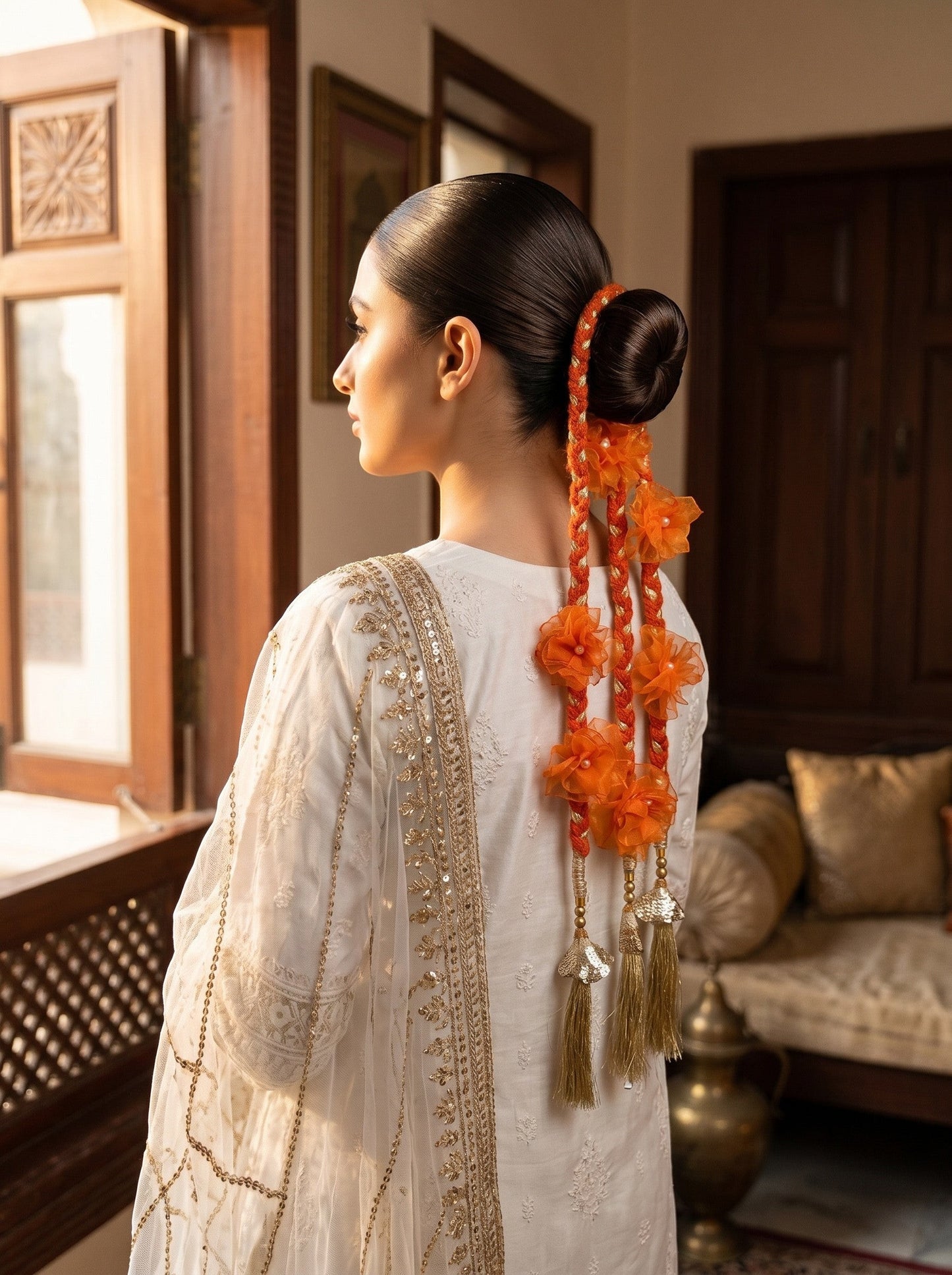 Lily Aamrass Blossom Paranda featuring orange floral accents and gold tassels worn on a sleek bun for ethnic style.