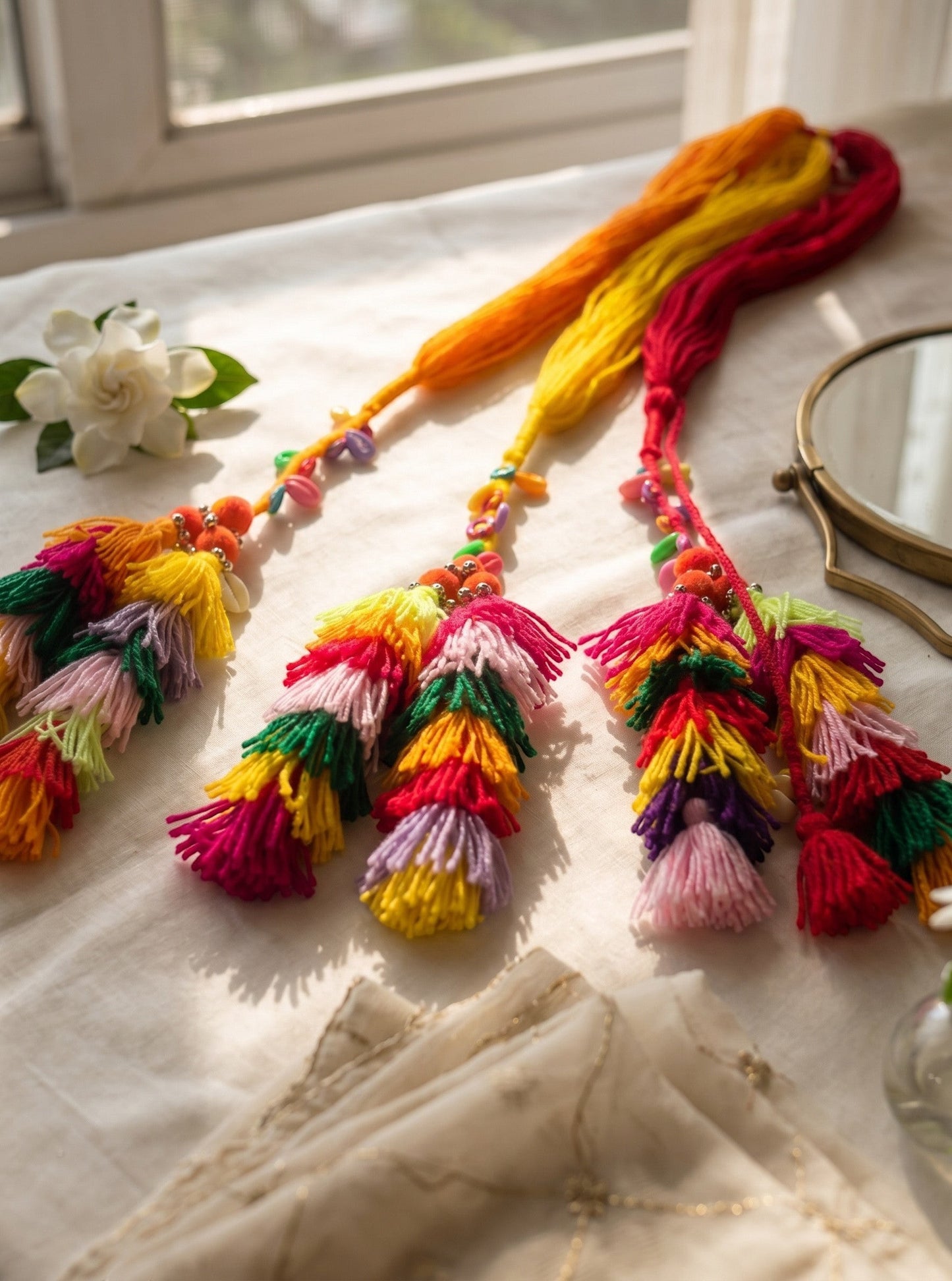 Lily Basanti Paranda hair accessory featuring vibrant multi-colored yarn tassels, beads, and pom-poms on a table.