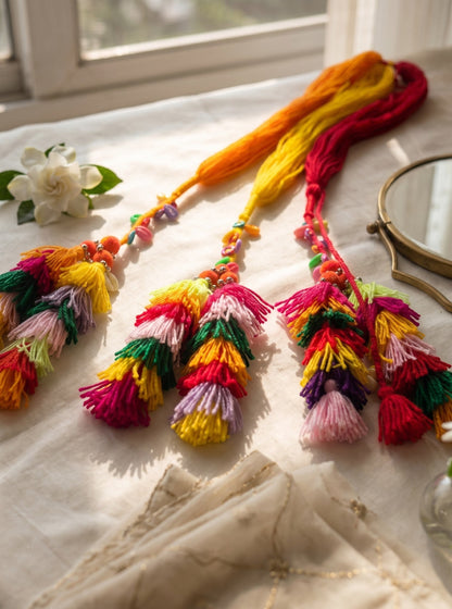 Lily Basanti Paranda hair accessory featuring vibrant multi-colored yarn tassels, beads, and pom-poms on a table.