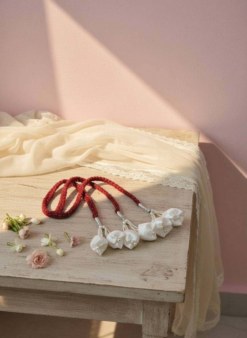 Lily beaded garland with fabric flower embellishments, deep red braided cords, silver beads, and white fabric flowers.