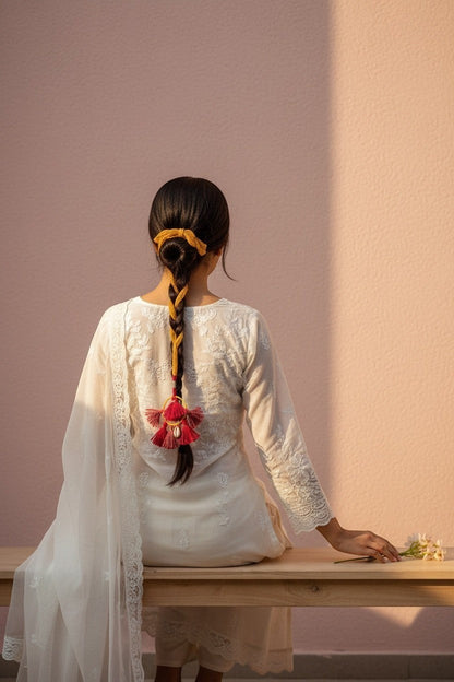 Lily bohemian tassel hair accessory with deep magenta and mustard yellow threads, shell accents, and yellow bow, braided into hair.