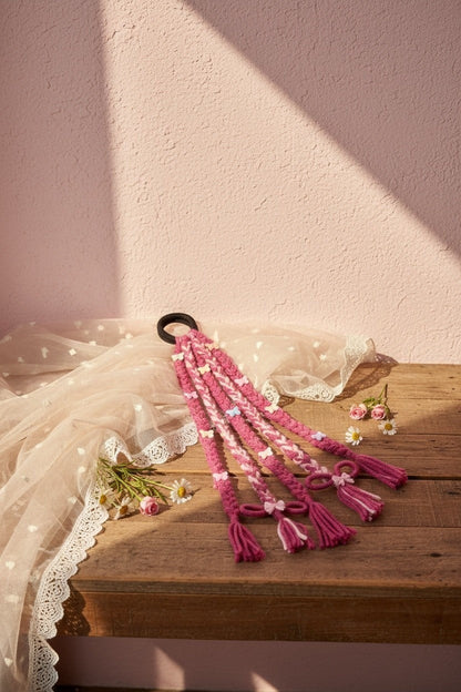 Lily pink and white braided hair accessory with butterfly charms, bows, and tassels attached to an elastic band.