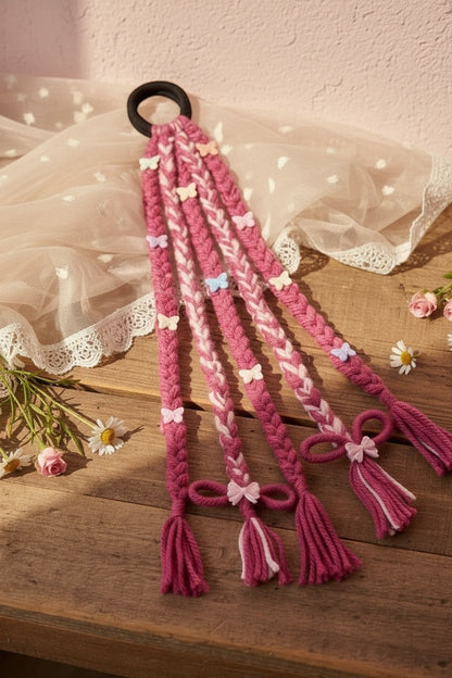 Lily braided hair accessory in pink and white yarn with butterfly charms, bows, and tassels attached to an elastic band.