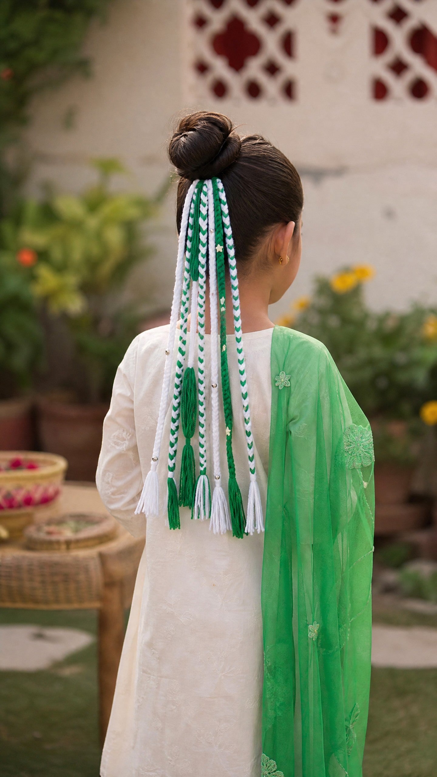 Lily handcrafted braided hair accessory with green and white threads, tassels, and star charms on a woman's bun.