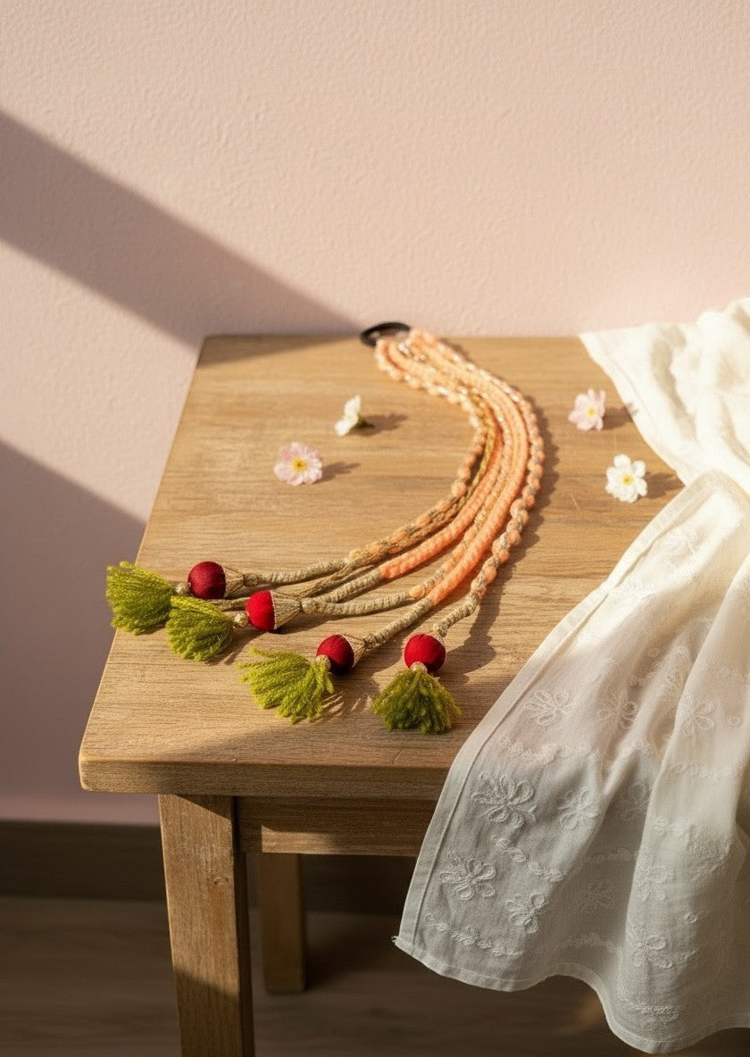 Lily braided hair accessory with peach, beige yarn, red beads, and lime green tassels. Bohemian style.