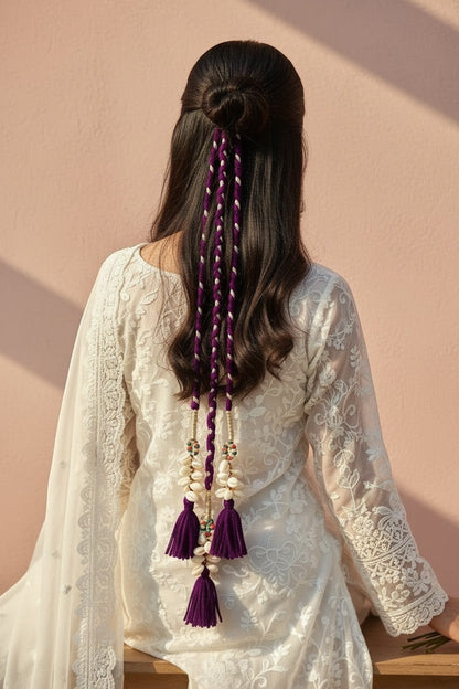 Lily braided purple and white hair accessory with shells, beads, and tassels, worn by a woman with dark hair.