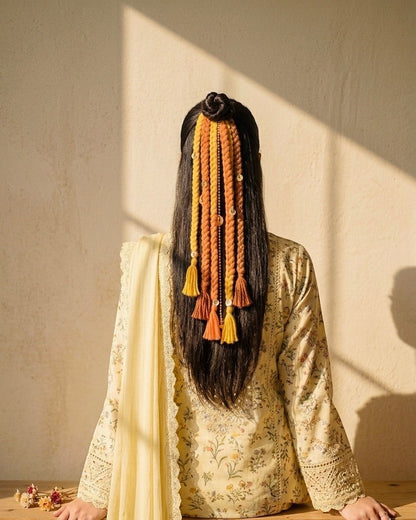 Lily braided hair accessory with yellow, orange, and brown yarn, beads, and tassels. Styled in a bun with loose braids.