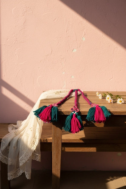 Lily braided hair accessory with teal and fuchsia tassels and decorative charms.