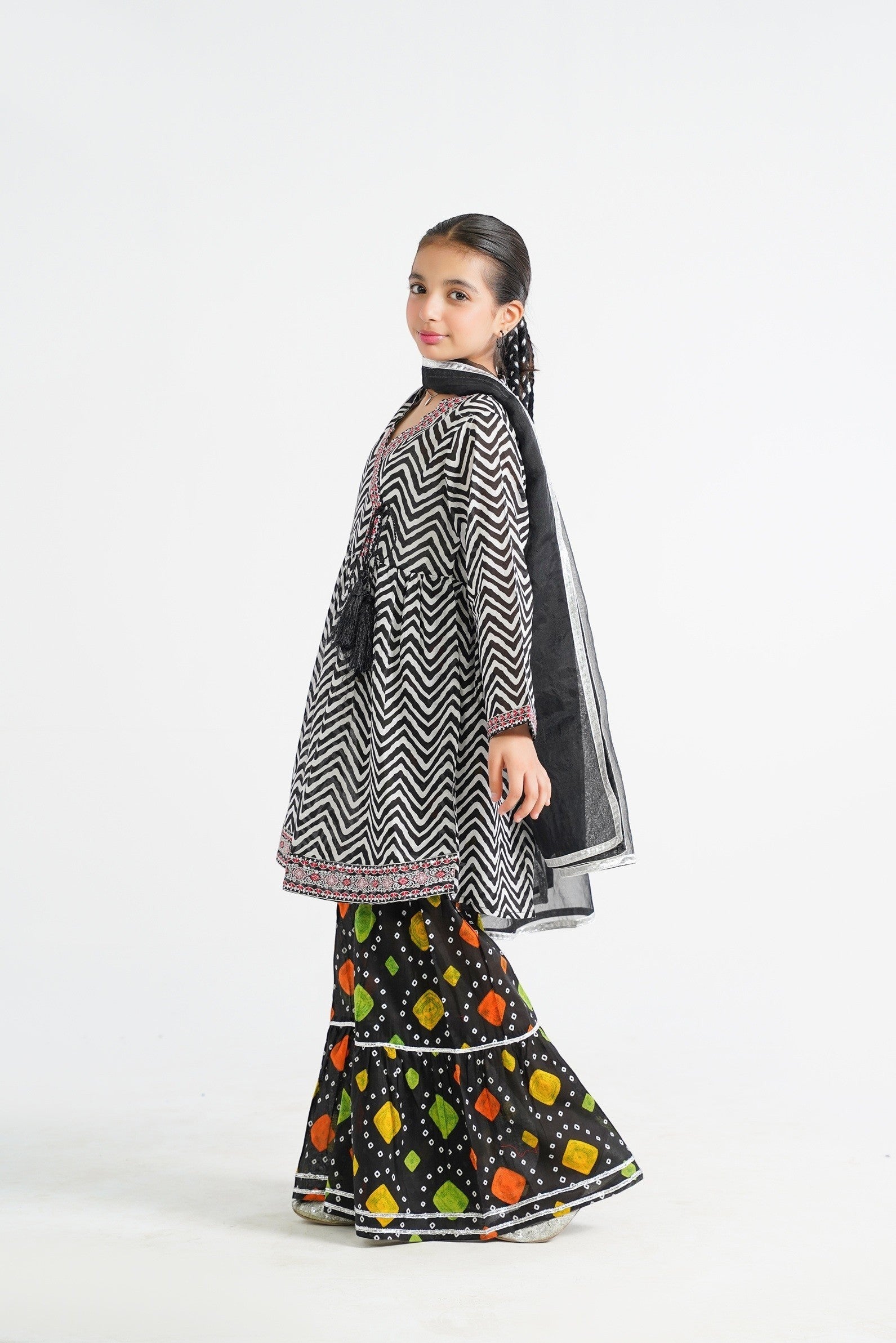 Lily black and white zigzag print kurta with red embroidery and tassels, paired with colorful tiered sharara and black dupatta.