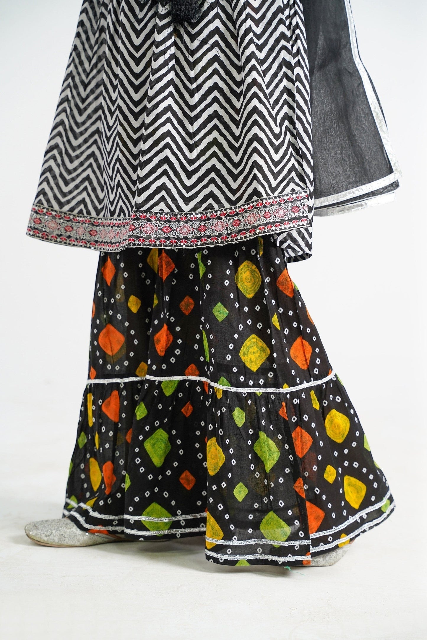 Lily black and white zigzag print kurta with red embroidery and black tassels, paired with a colorful tiered sharara and black dupatta.
