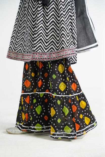 Lily black and white zigzag print kurta with red embroidery and black tassels, paired with a colorful tiered sharara and black dupatta.