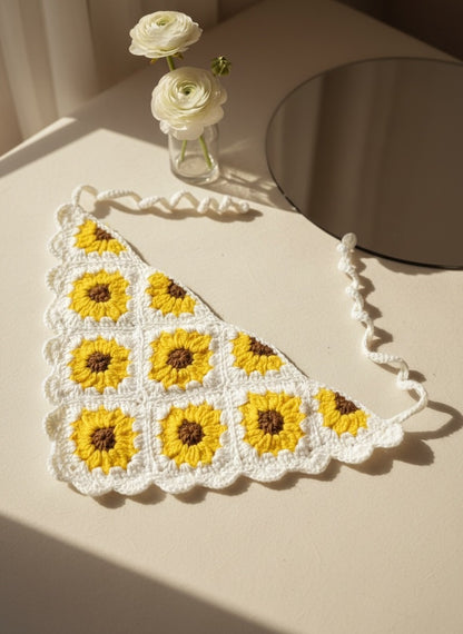 Lily handmade crochet sunflower hair bandana in yellow and white with tie-back straps on a neutral surface.