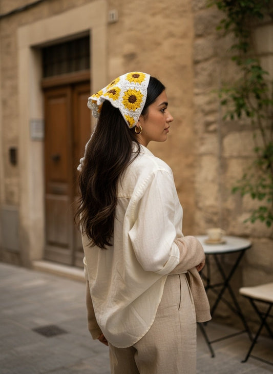 Lily handmade crochet sunflower headscarf in yellow and white worn by a woman on a cobblestone street