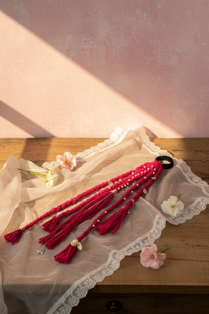 Lily braided fuchsia yarn hair accessory with pearls, tassels, and charms attached to a hair tie.