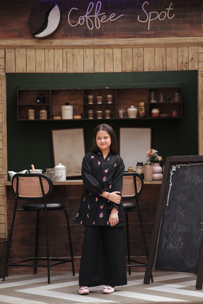 Lily girls black tunic and trouser set with multi-colored floral embroidery, V-neck, and ruffled cuffs in a cafe