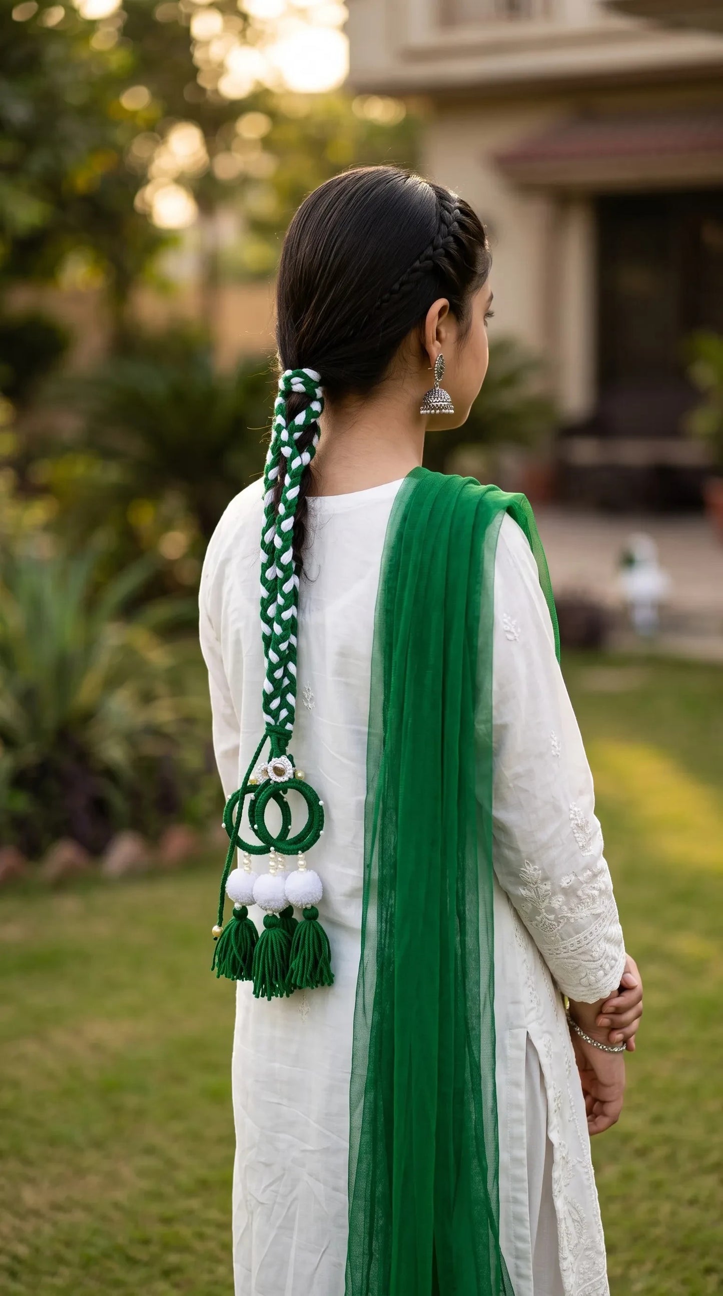 Lily Green Glory Traditional Paranda braided into hair with white pom-poms and green tassels on a woman in a white outfit.
