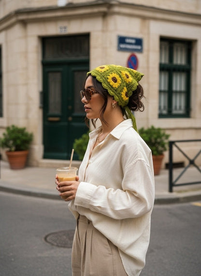 Lily green crochet hair bandana with yellow sunflower motifs worn by a woman in a white shirt on a city street