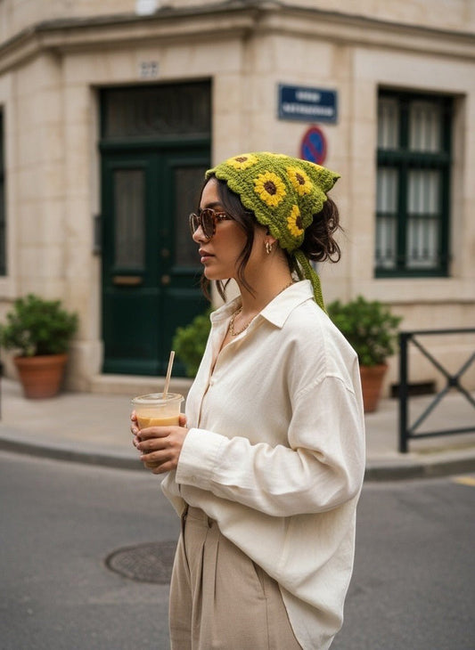 Lily green crochet hair bandana with yellow sunflower motifs worn by a woman in a white shirt on a city street