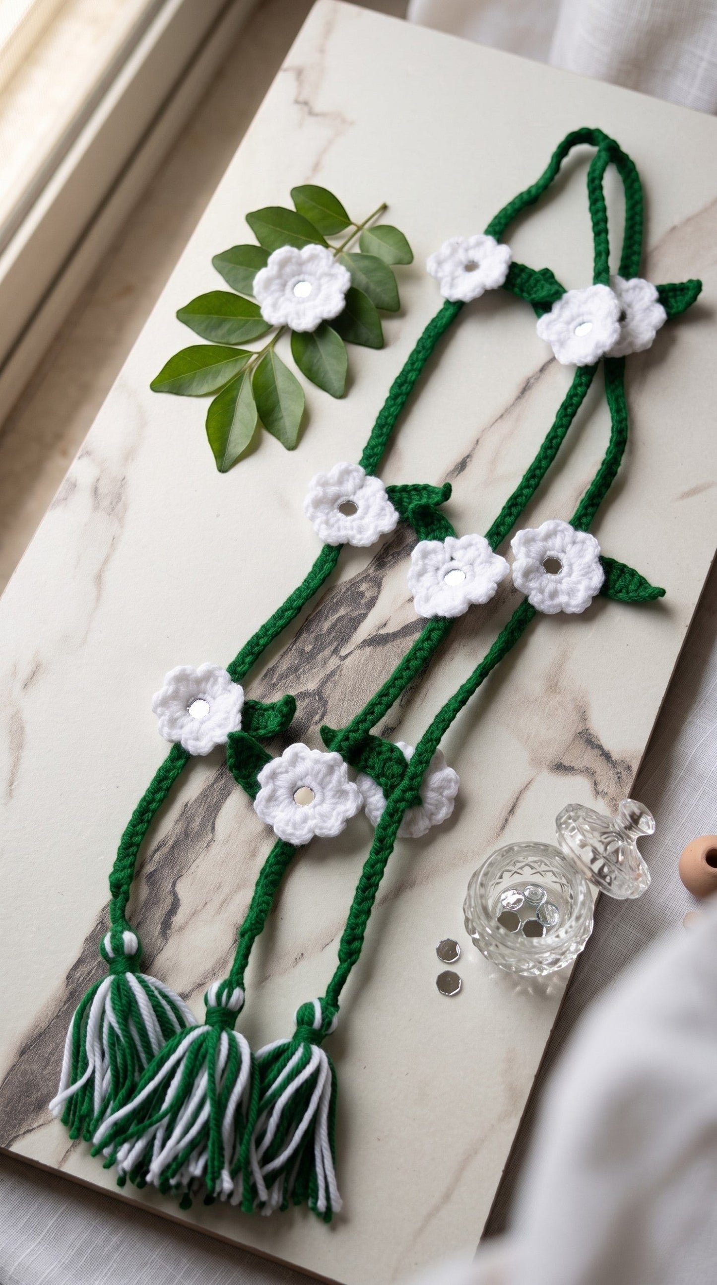 Lily green and white crocheted flower hair braids with mirror accents and tassels on a marble surface.