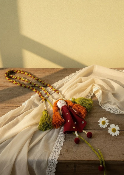 Lily handmade fabric doll necklace with red polka dot dress, orange yarn hair, green tassels, and red pom-pom feet.