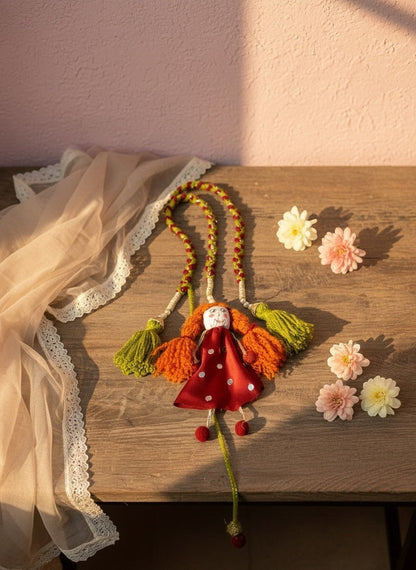 Lily handmade fabric doll necklace with red polka dot dress, orange yarn hair, green tassels, and red pom-pom feet.