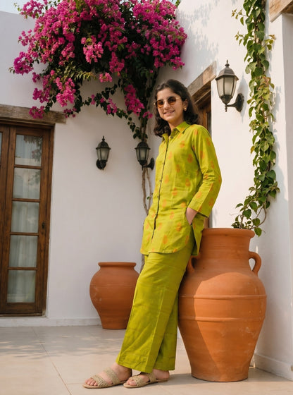 Lily lime green long sleeve shirt and wide leg trouser set with orange pattern worn by a woman in a sunny courtyard.