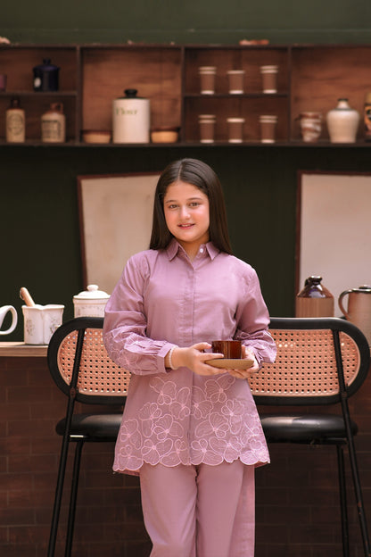 A young girl wearing a Lily mauve long-sleeved button-down shirt and trousers with delicate floral embroidery.