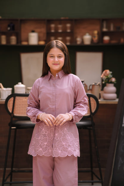 A young girl wearing a Lily mauve long-sleeved button-down shirt and trousers with delicate floral embroidery.