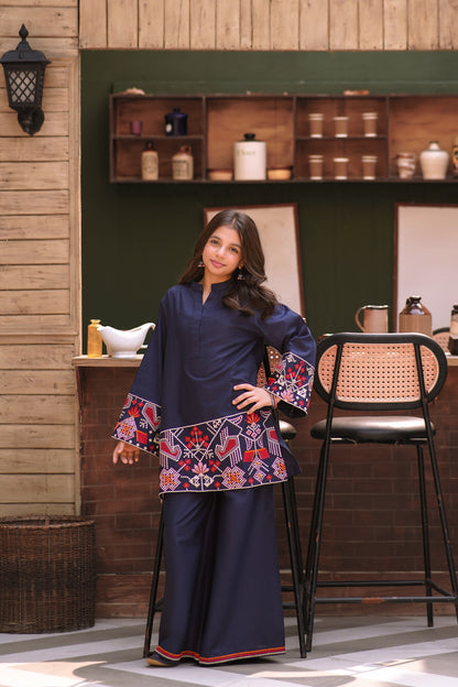 Lily navy blue two-piece kurta set with multi-colored geometric embroidery on a young girl in a rustic kitchen.