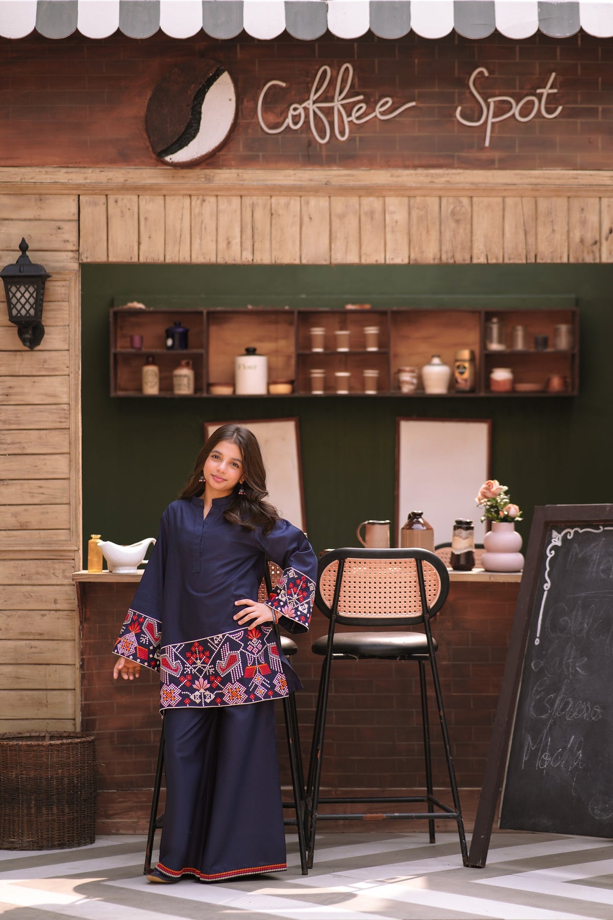 Lily navy blue two-piece kurta set with geometric embroidery on sleeves and hem worn by a girl in a cafe setting.