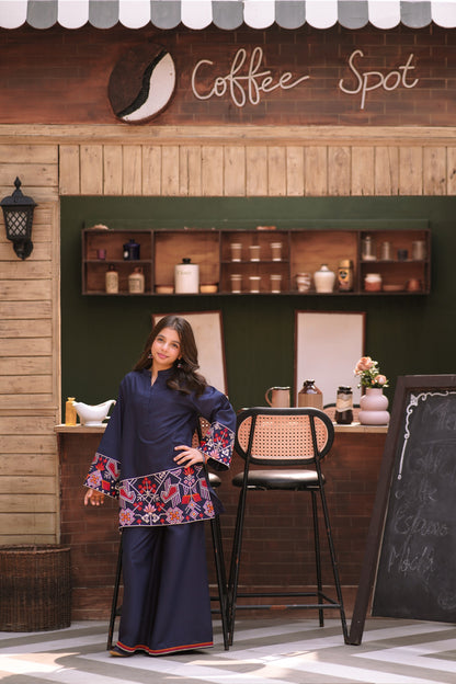 Lily navy blue two-piece kurta set with geometric embroidery on sleeves and hem worn by a girl in a cafe setting.