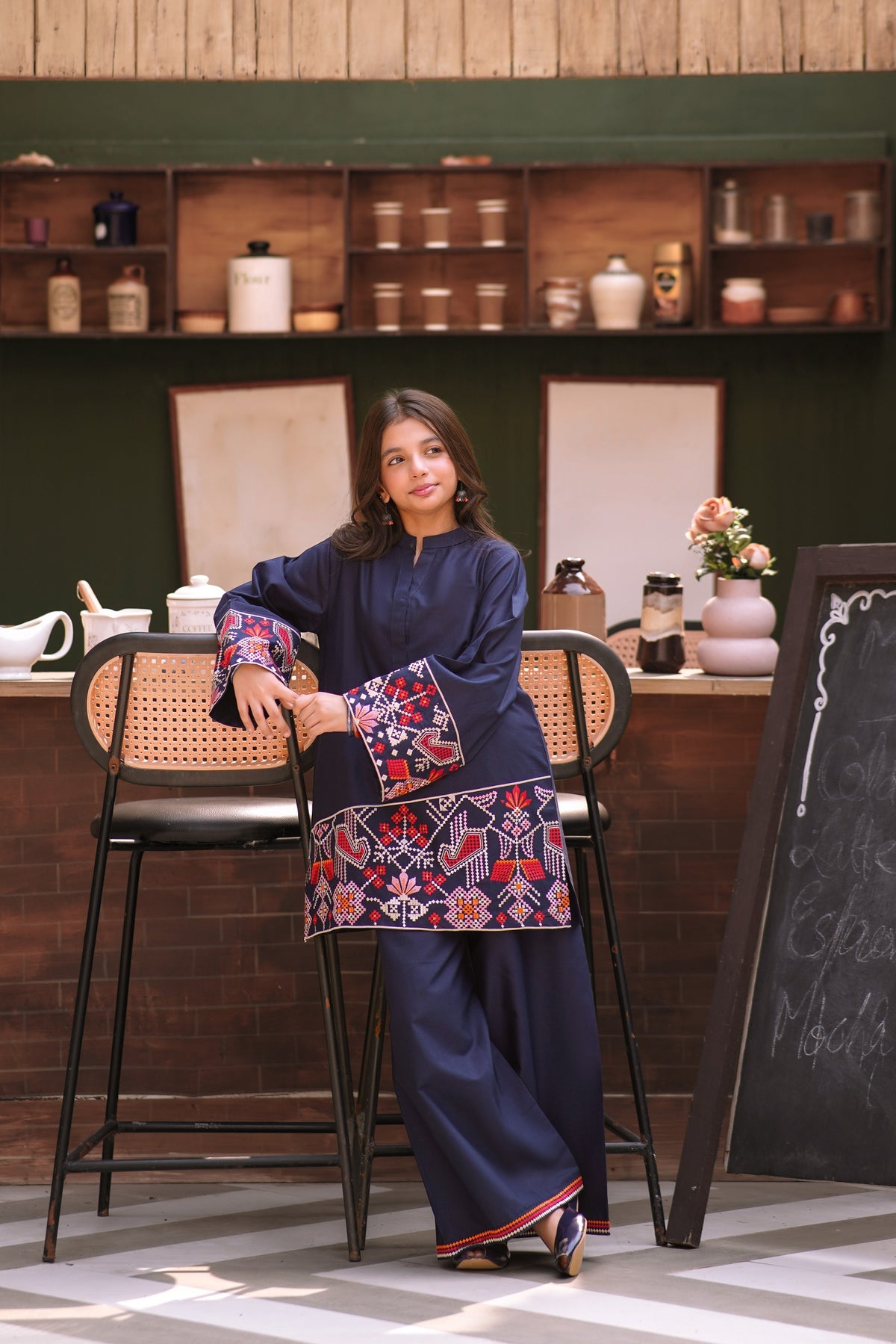 Lily navy blue two-piece kurta set with geometric embroidery on sleeves and hem worn by a young girl in a cafe.