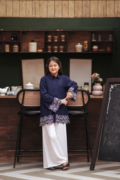 Lily navy blue button-down tunic with white floral embroidery on cuffs and hem, worn by a girl with white trousers.