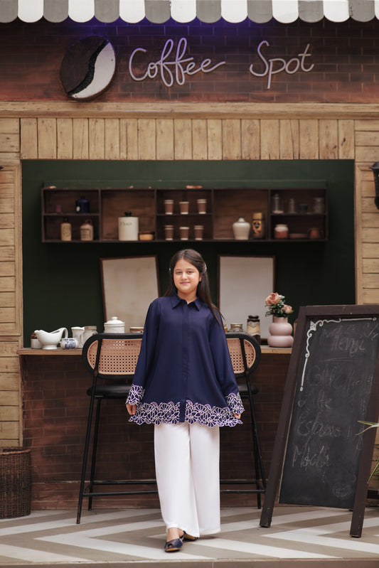 A girl wearing a Lily navy blue long sleeve button-down tunic with white floral embroidery on the cuffs and hem.