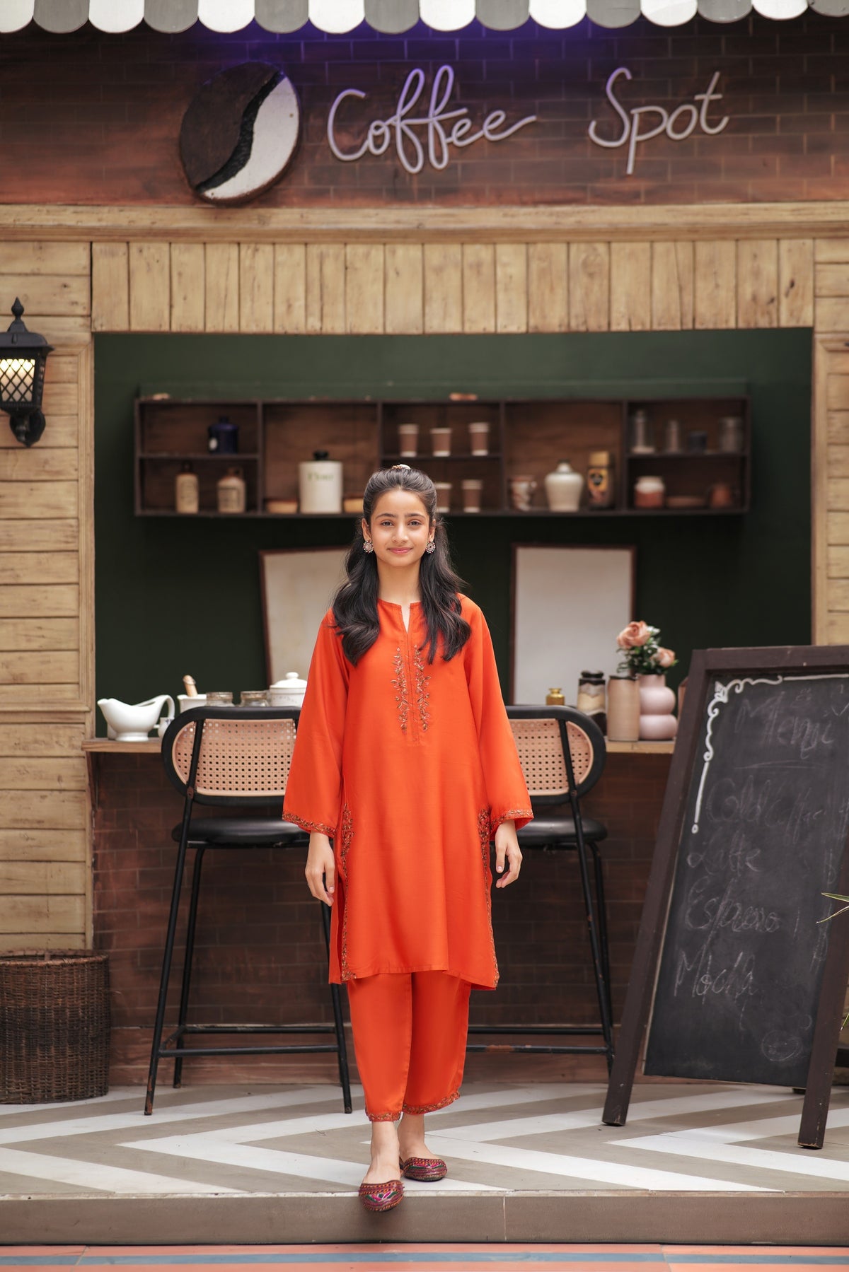 Lily girl wearing a vibrant orange embroidered kurta and trouser set with floral detailing at a coffee shop