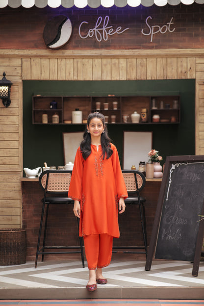 Lily girl wearing a vibrant orange embroidered kurta and trouser set with floral detailing at a coffee shop