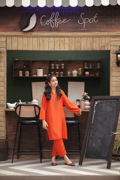 Lily girl wearing a vibrant orange embroidered kurta and trouser set with floral details in a coffee shop setting