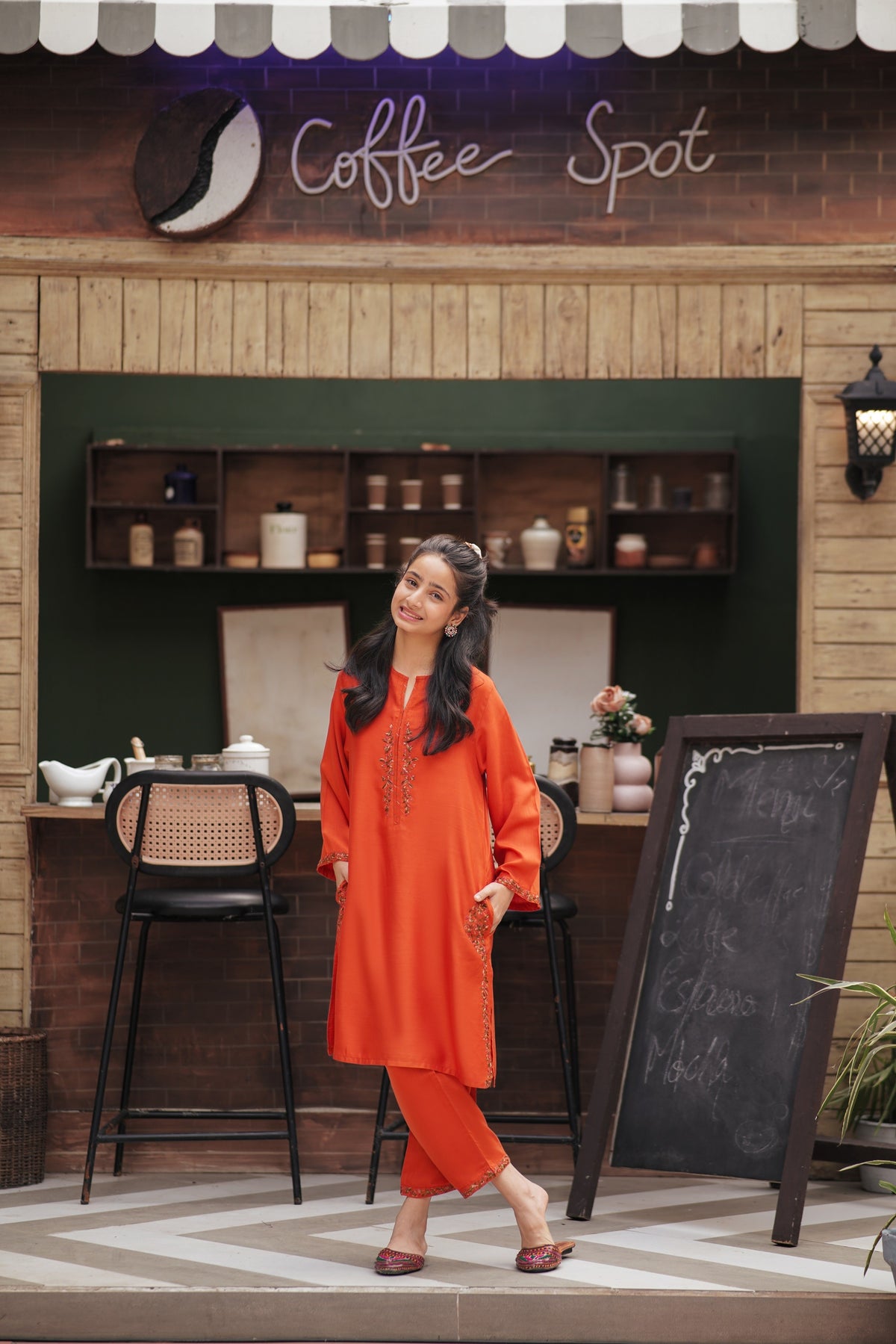 Lily orange embroidered kurta and trouser set worn by a smiling girl in a cafe setting